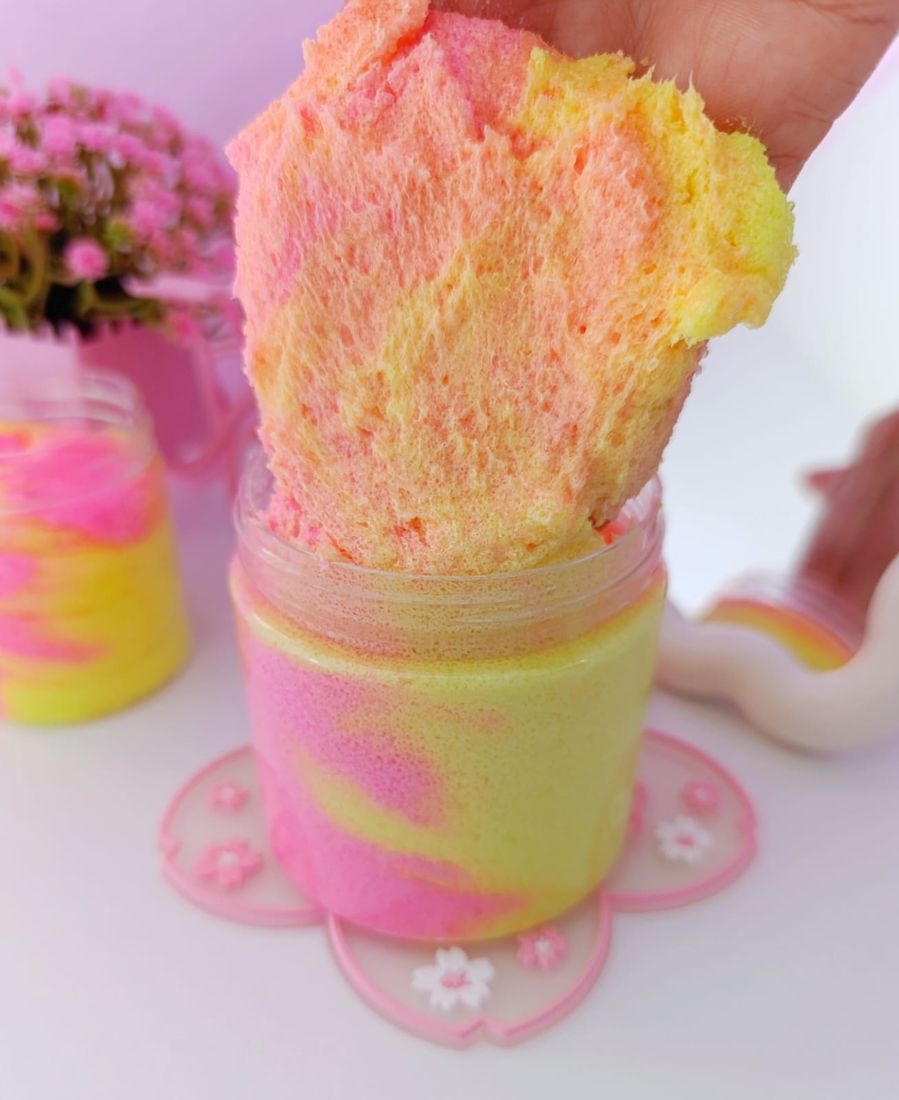 Mano sosteniendo exfoliante batido rosa y amarillo